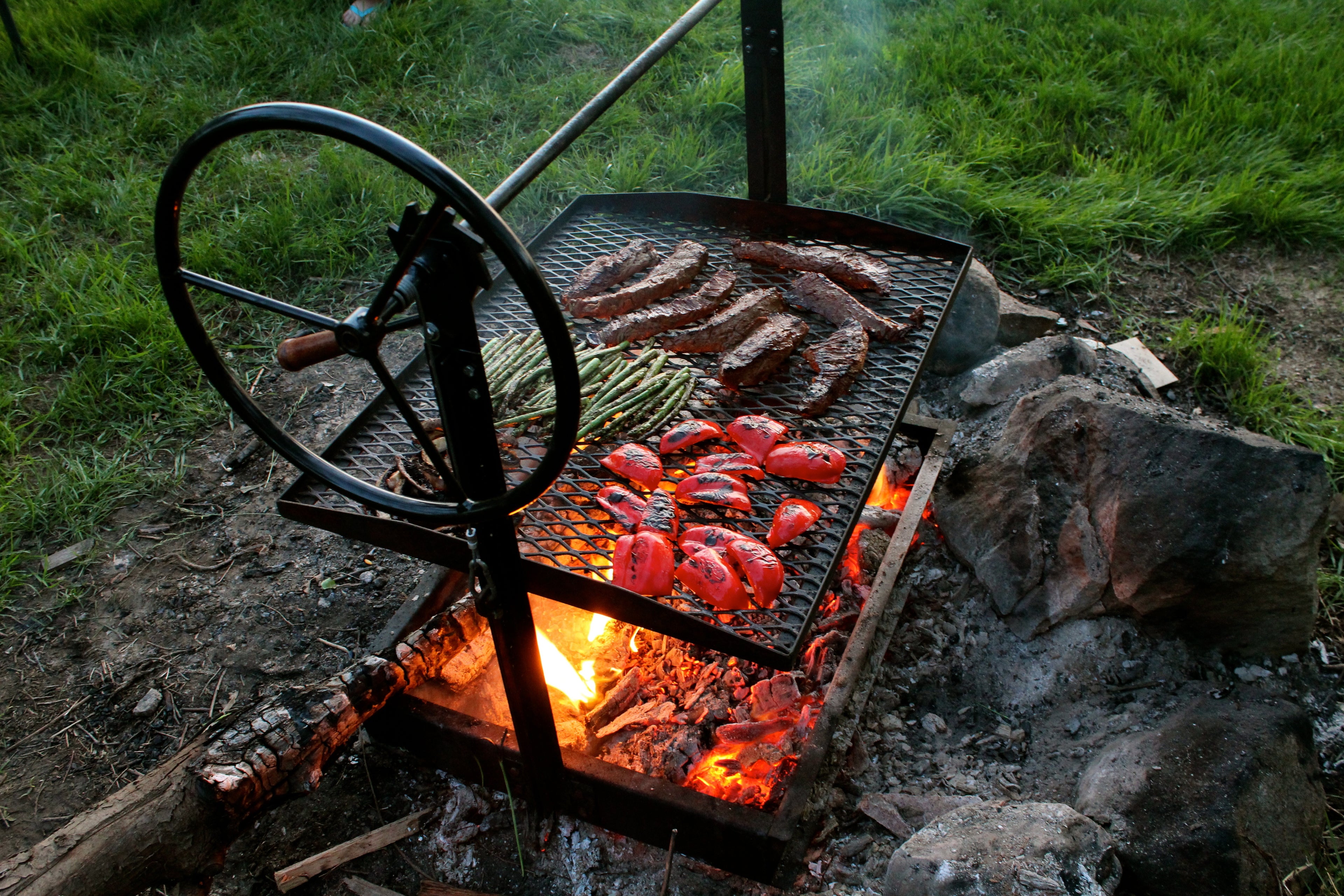 Original Braten Campfire grill being used on an open fire pit with food cooking on top